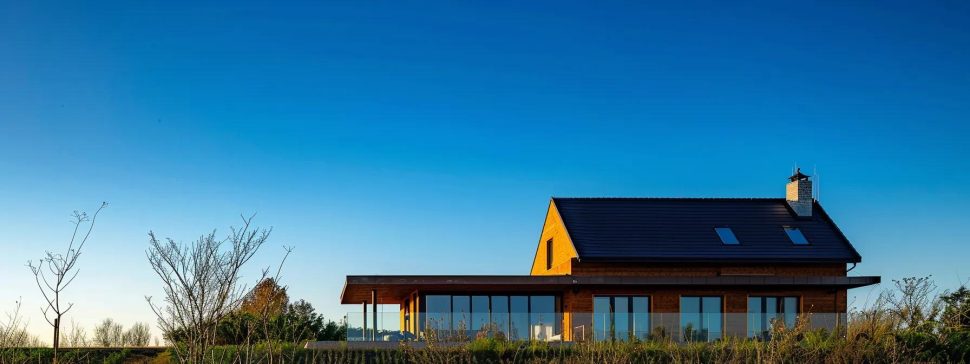 a modern, sleek house with a shiny synthetic roof contrasting with a rustic cottage with a natural thatched roof, both under a clear blue sky.
